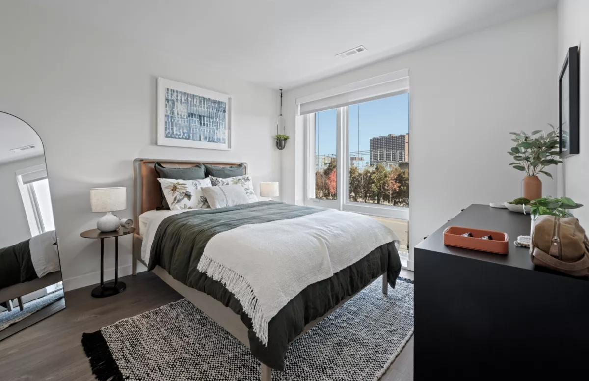 Bright bedroom with large window, green bedding, and modern minimalist decor.