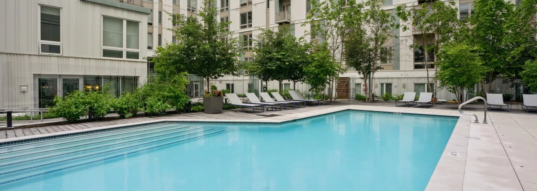 Outdoor pool with lounge chairs surrounded by modern apartment buildings.