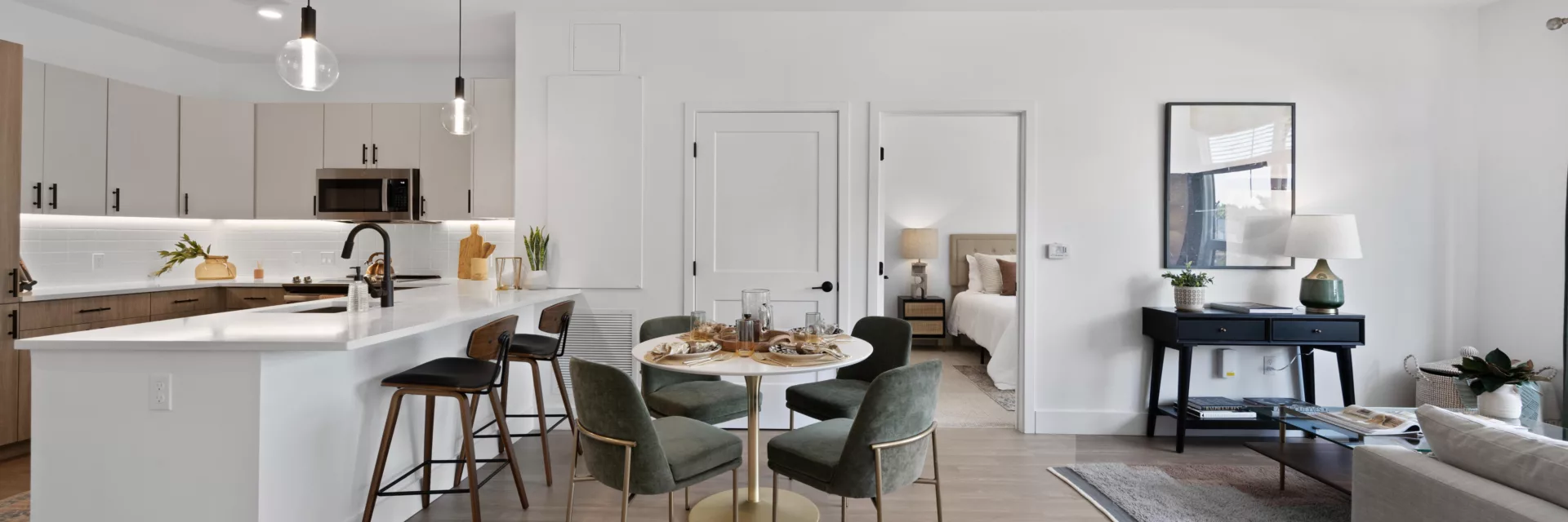 Dining area with round table and dark green chairs, next to the kitchen counter with high stools.