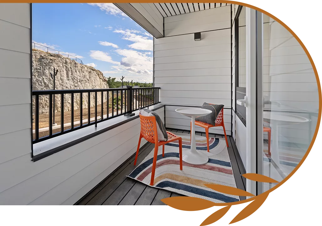 Covered balcony with two orange chairs, white table, and view of rocky cliffside