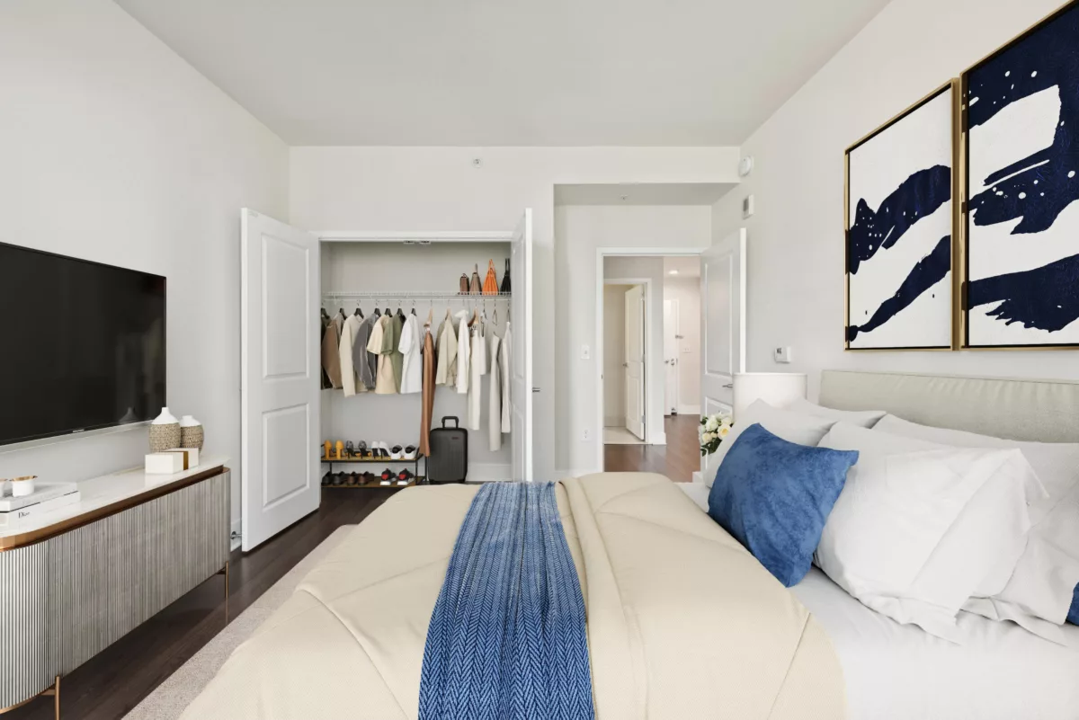 Bedroom with open closet, neutral bedding, and abstract wall art.