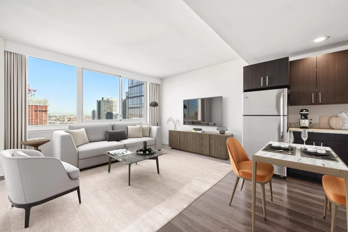 Open concept kitchen with dark cabinets and living room with white sofa and chair with large windows overlooking a city.