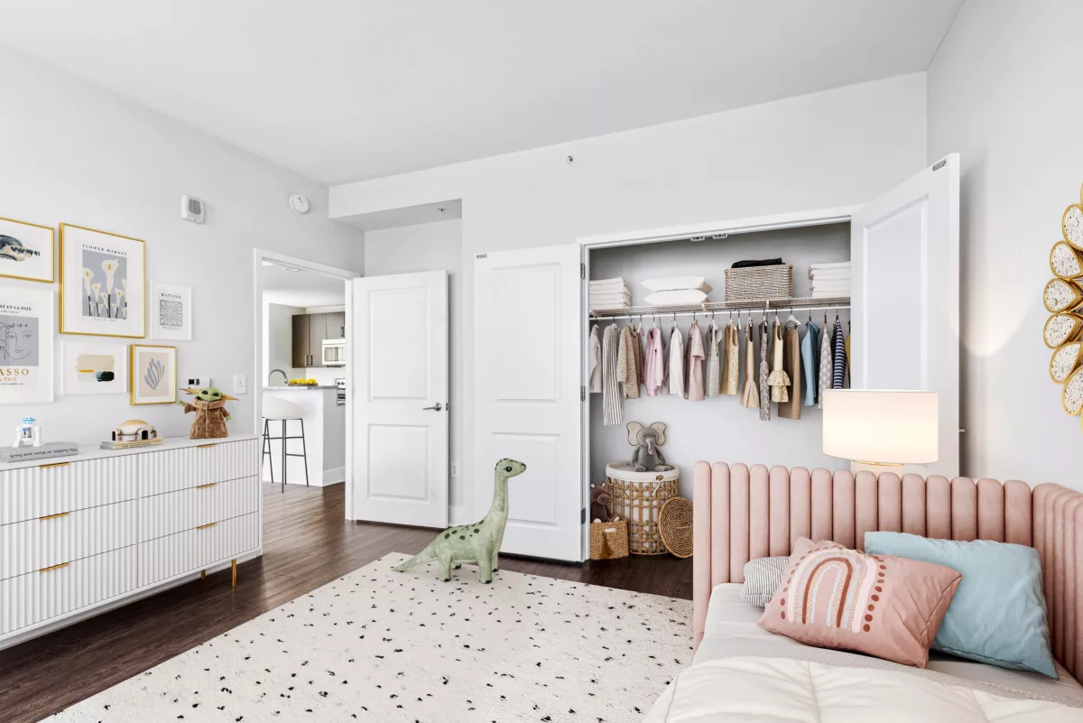 Child’s bedroom with pink bed, toy dinosaur, and open closet.
