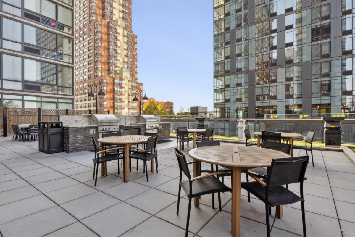 Rooftop patio with dining tables, grills, and surrounding high-rises.