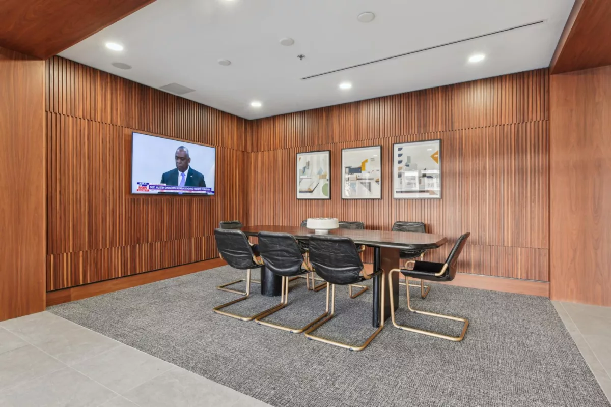 Conference room with long table, TV on wood-paneled wall, and modern artwork.