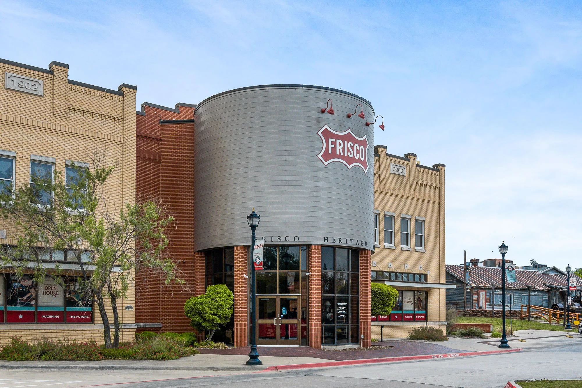 A building with beige and red brick with a large "Frisco" sign over the entrance with a parking lot in front.