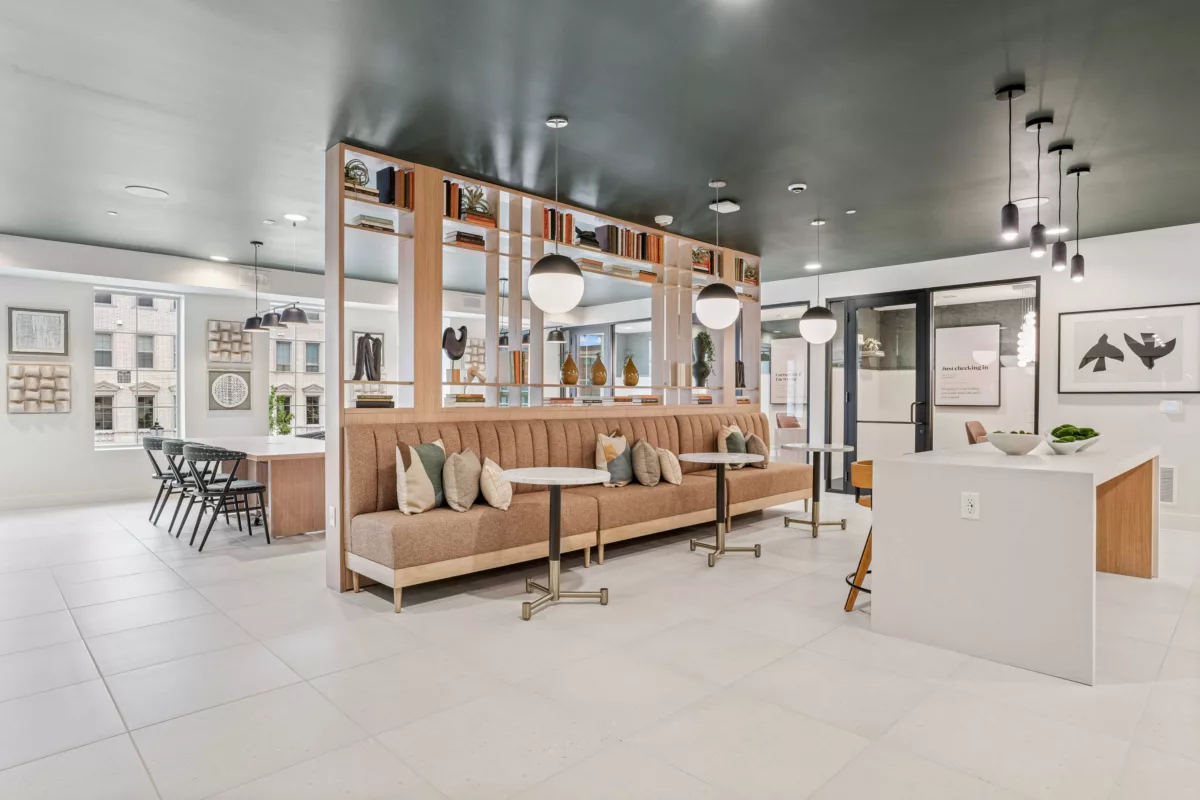 Coworking space with banquette seating, tables, open shelving, and white tile flooring.