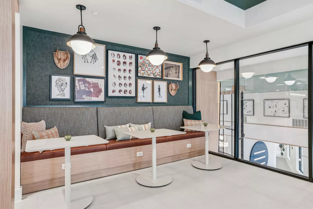 Coworking lounge with booth seating, tables, pendant lights, and framed artwork on a textured wall.