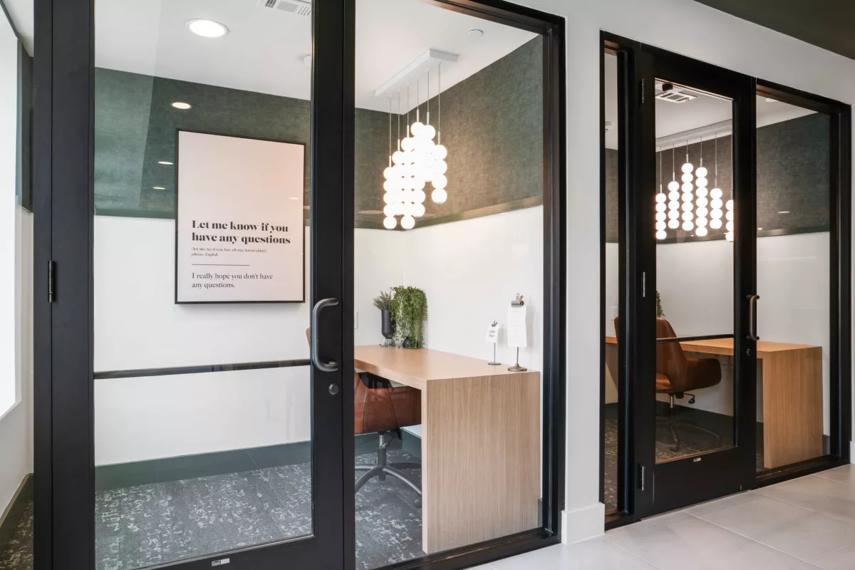 Private coworking office with desk, chair, and modern lighting fixture visible from hallway.