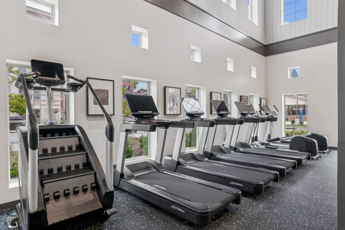 Fitness center with treadmills, stair climber, and elliptical machines in front of several windows.