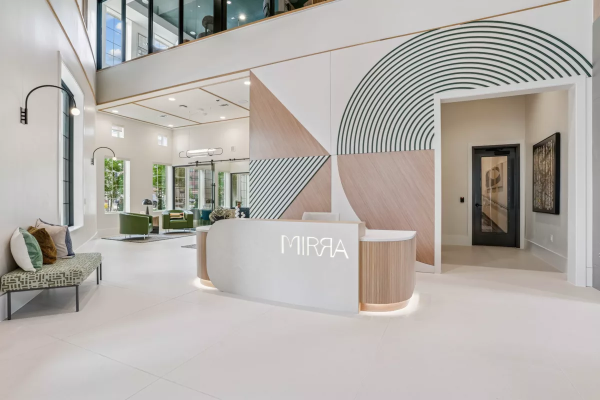Grand lobby with white reception desk and branded geometric wall design. Lounge seating available in front of the leasing center.