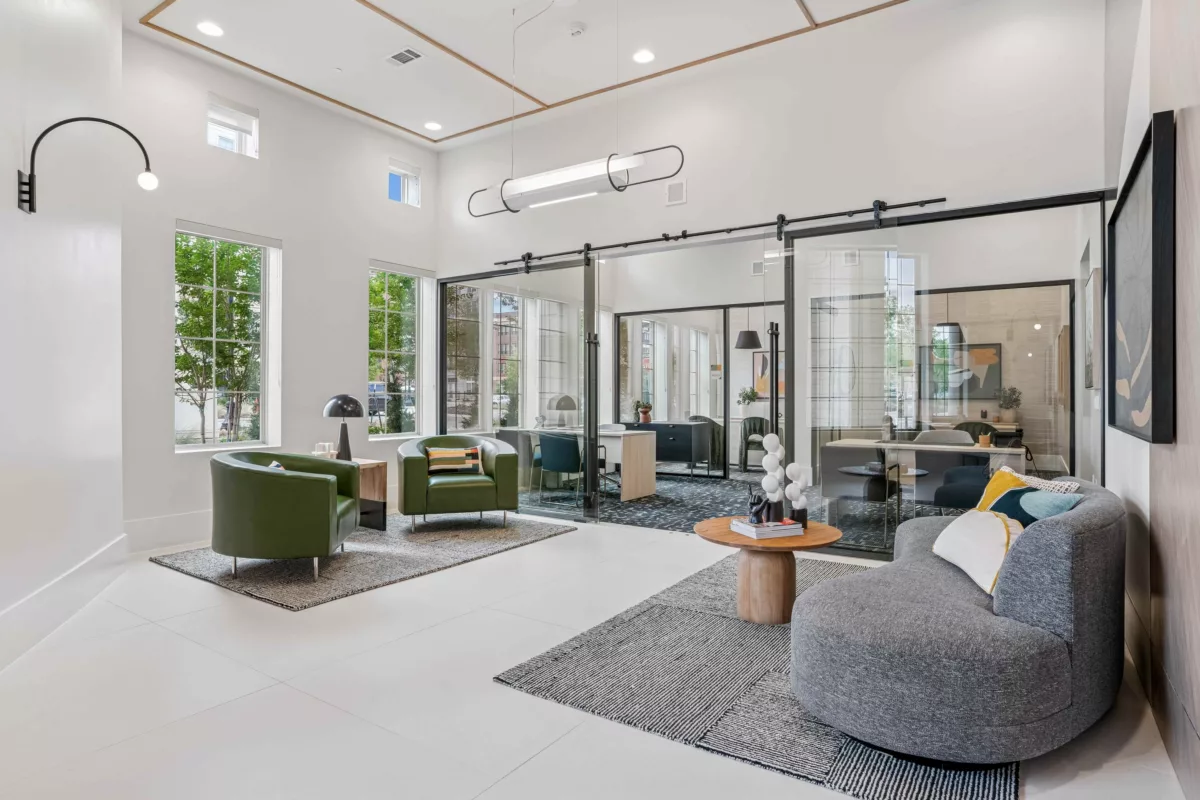 Leasing lounge with green chairs, gray sofa, and glass-enclosed office spaces.
