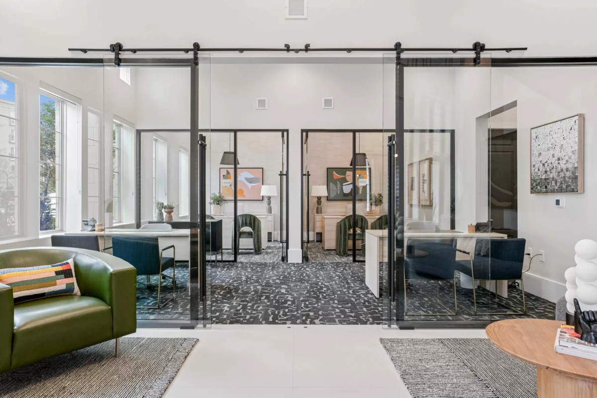 Leasing lounge with glass-enclosed offices, desks, chairs, and modern decor.
