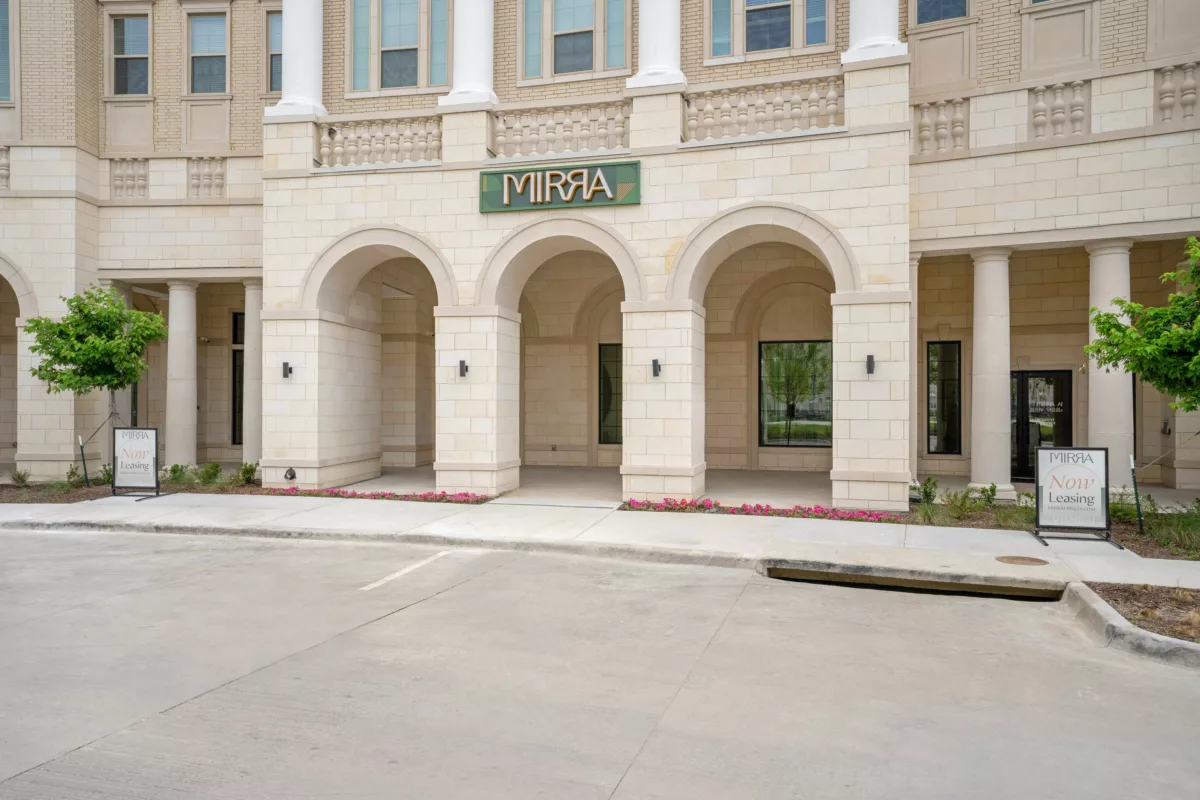 Building facade with arched entryway, columns, and stone detail with a sign that says "Mirra".