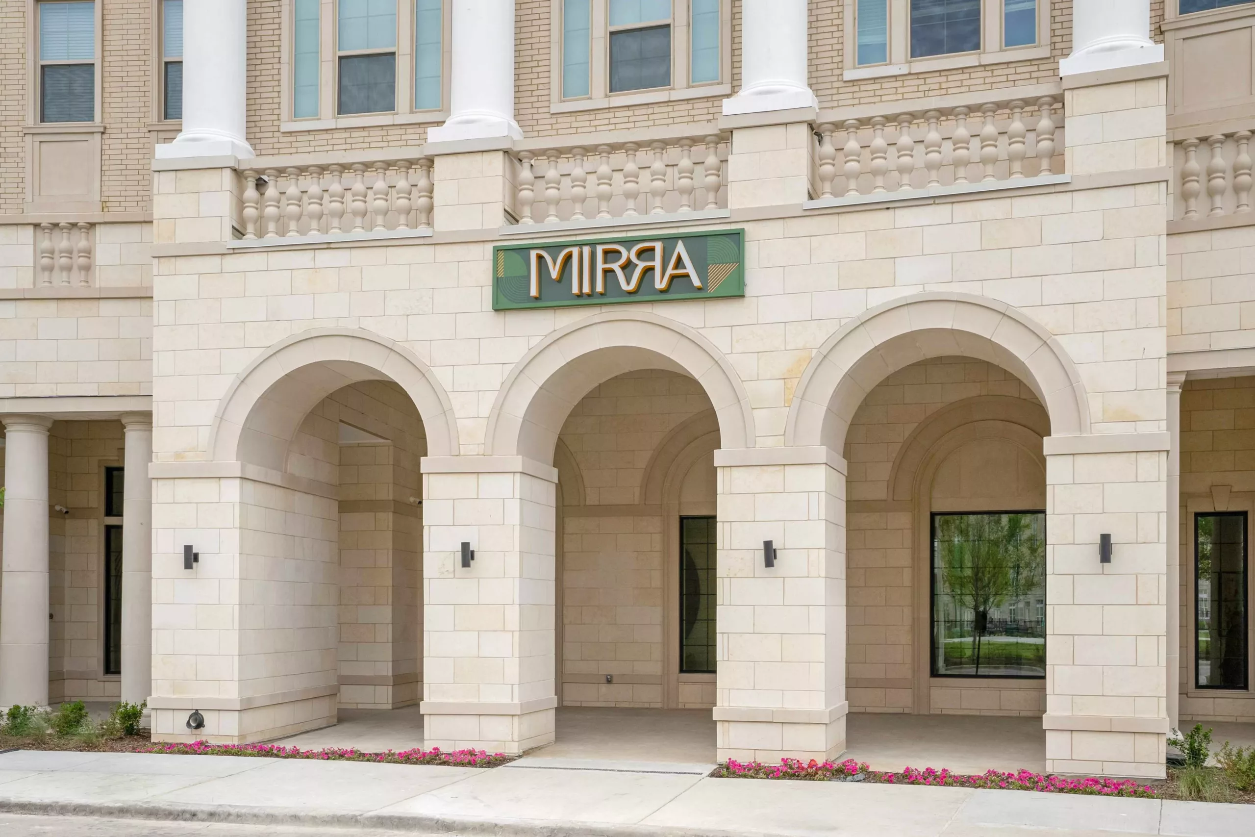 Building facade with arched entryway, columns, and stone detail with a sign that says "Mirra".
