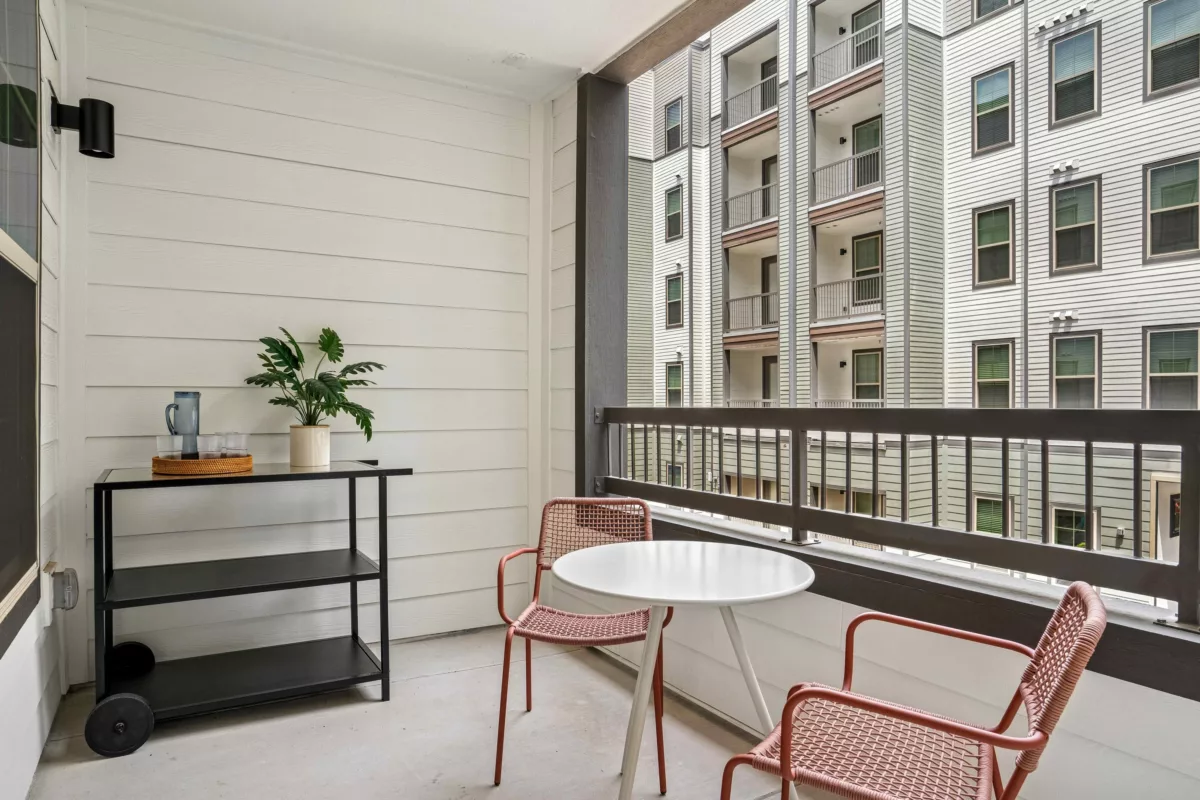Apartment balcony with table, chairs, and view of adjacent building.