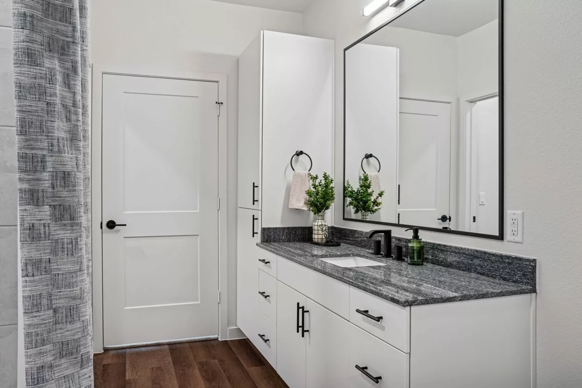 Modern bathroom with white vanity, granite countertop, black hardware, and framed mirror.