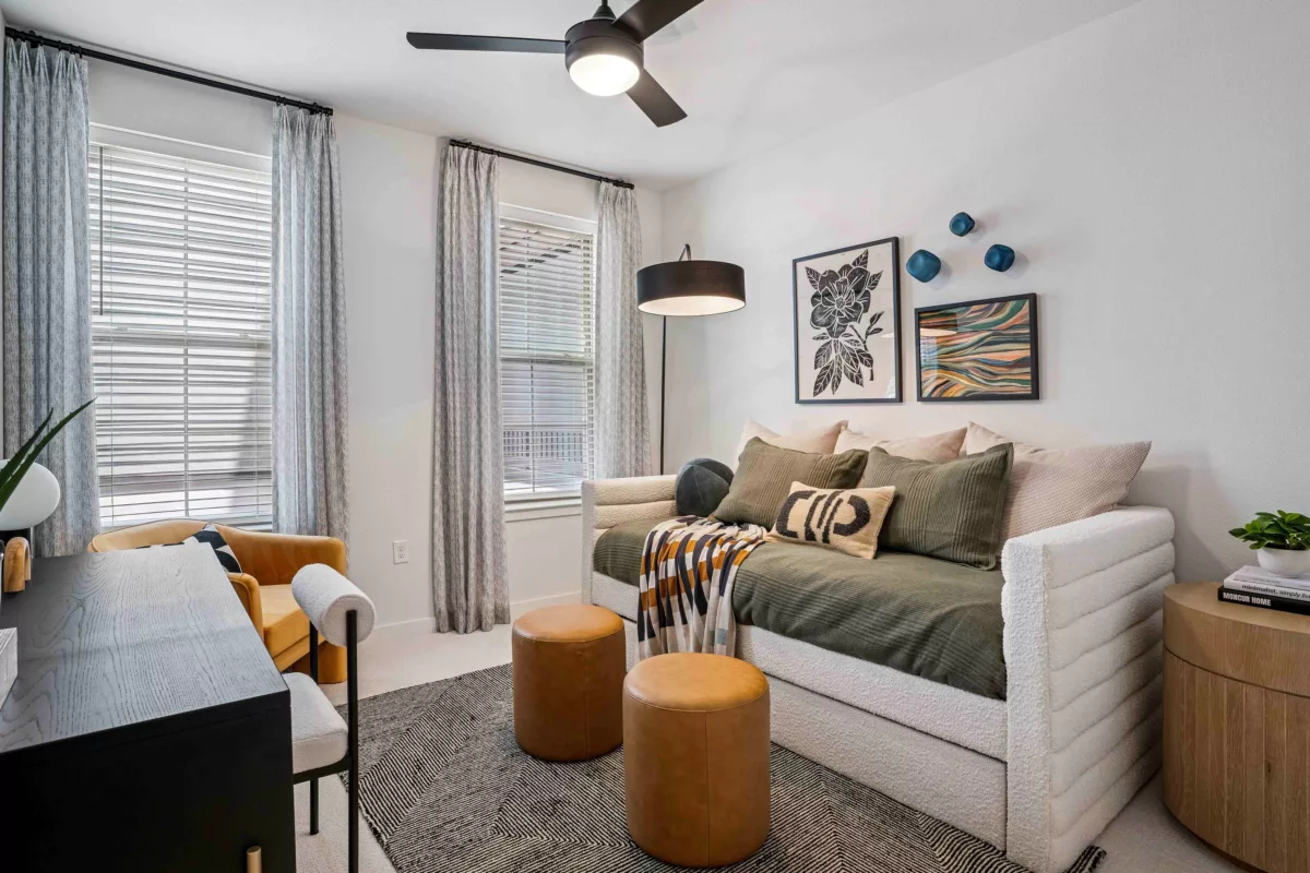 A bedroom with daybed, desk, chair, and leather ottomans on patterned rug.