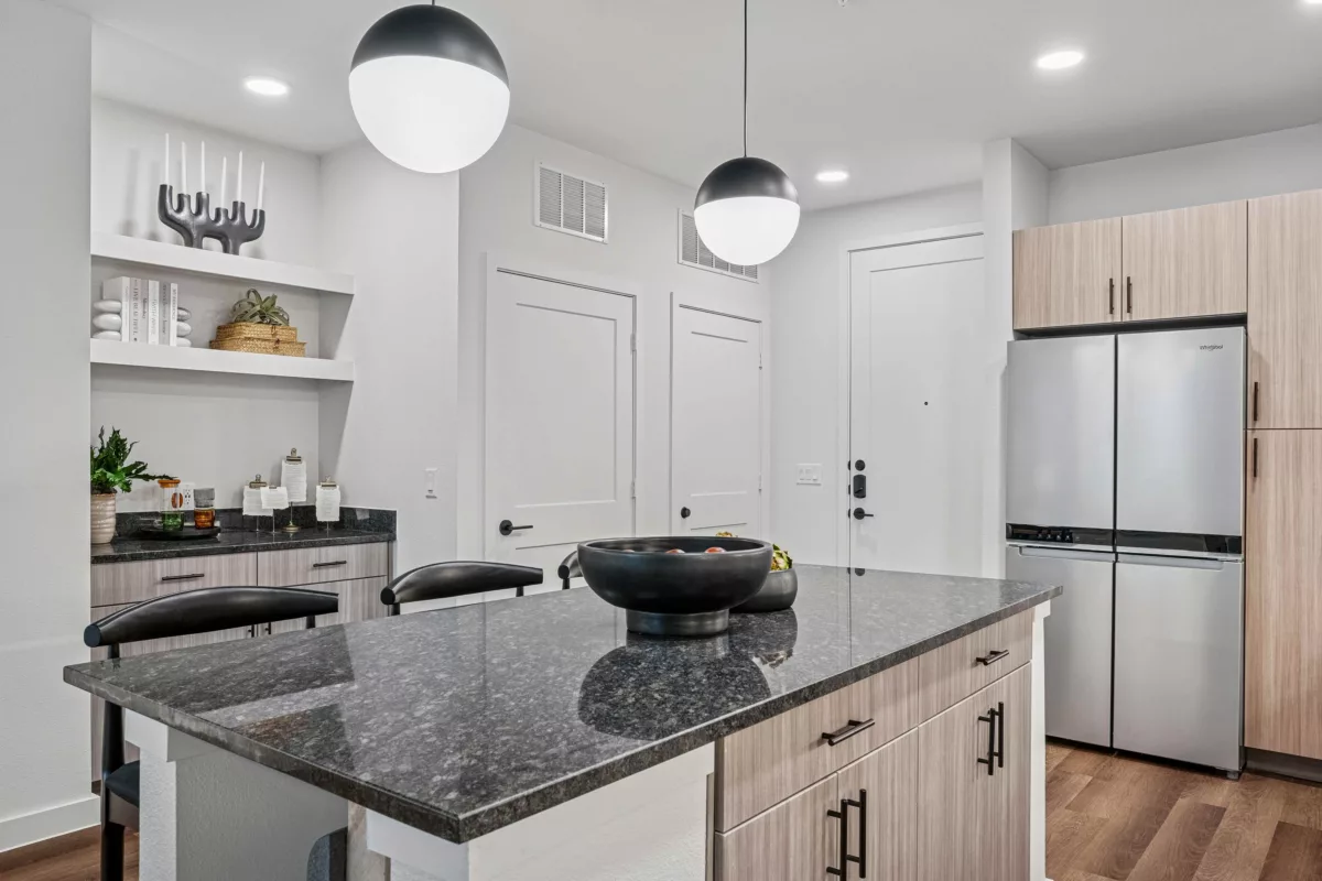 Kitchen with granite island, stainless steel refrigerator, and light wood cabinets.