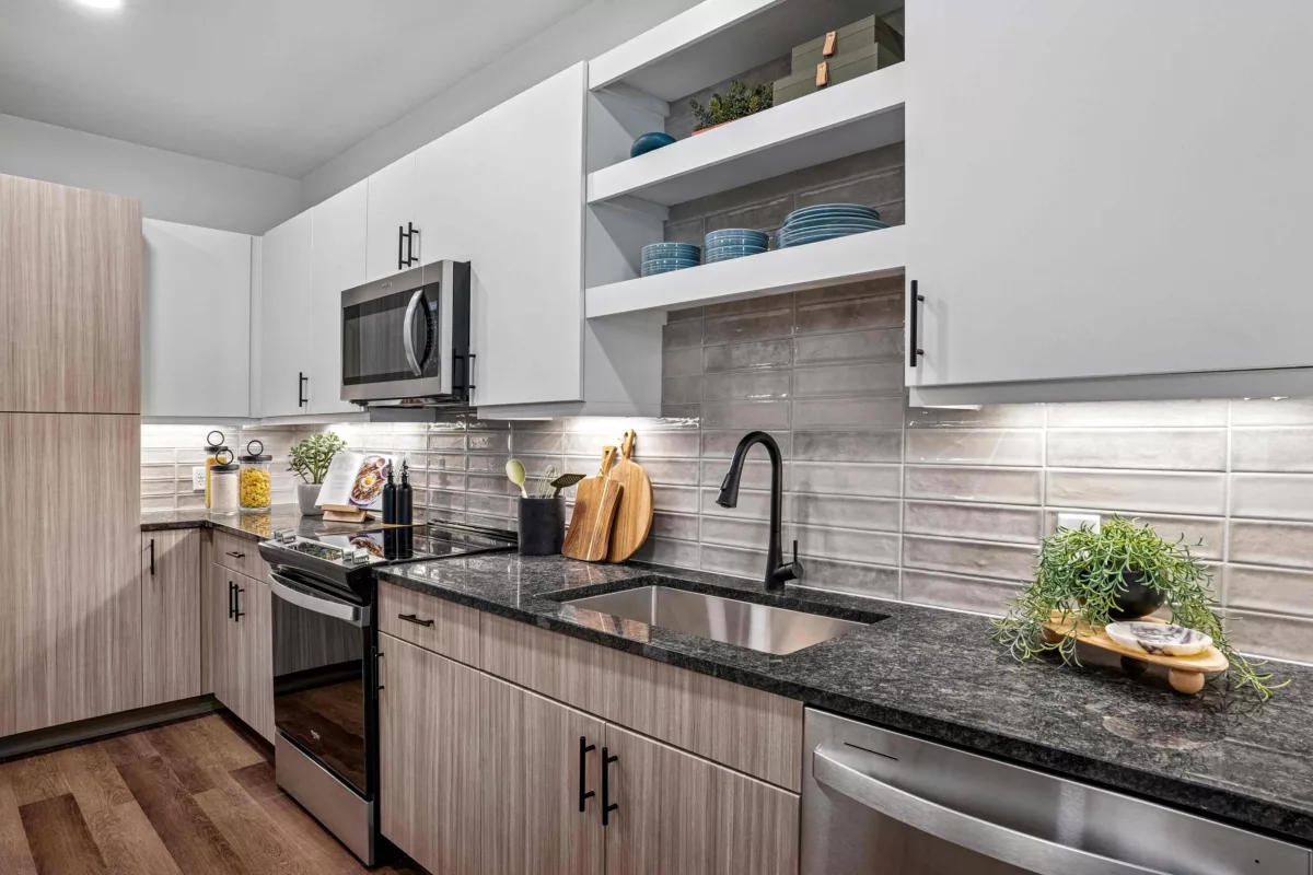 A modern kitchen with a stainless steel sink, black faucet, granite counters, and gray backsplash.