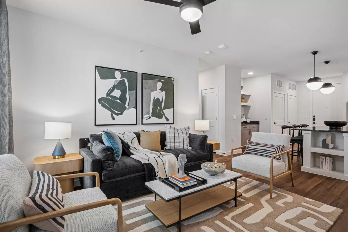 Modern living room with dark sofa, light chairs, and wood floors and artwork above couch.