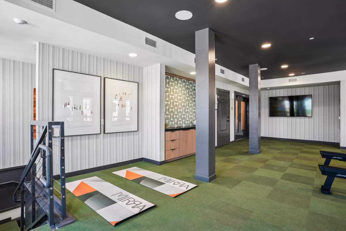 Fitness area with yoga mats, equipment, and mounted television on striped wallpaper.