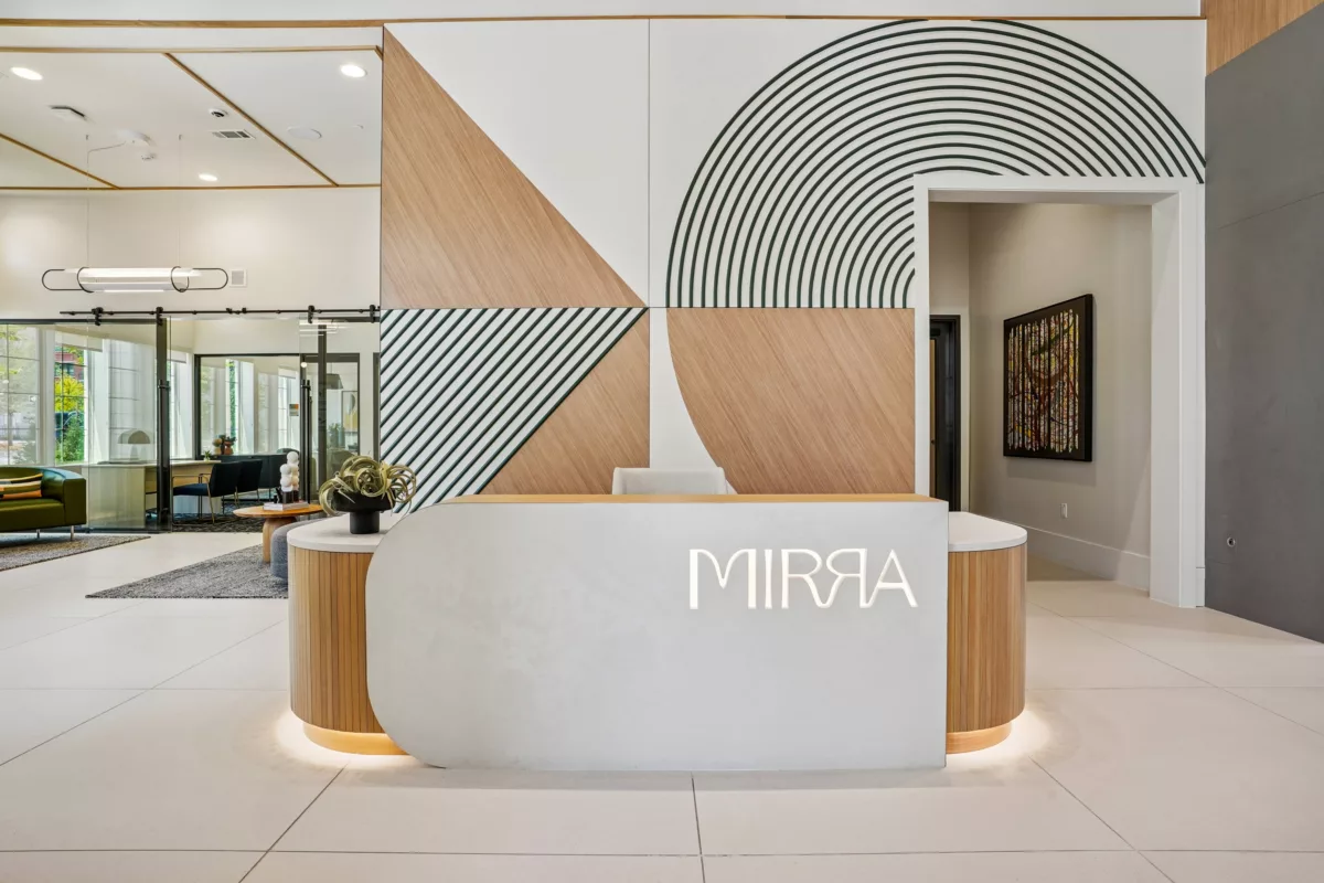 Grand lobby with reception desk, wood accents, and geometric wall design. Lounge seating available in front of leasing center.