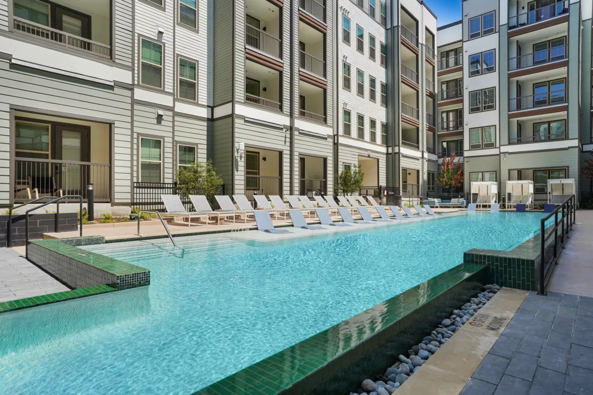 Outdoor pool with lounge chairs and multi-story building in the background.