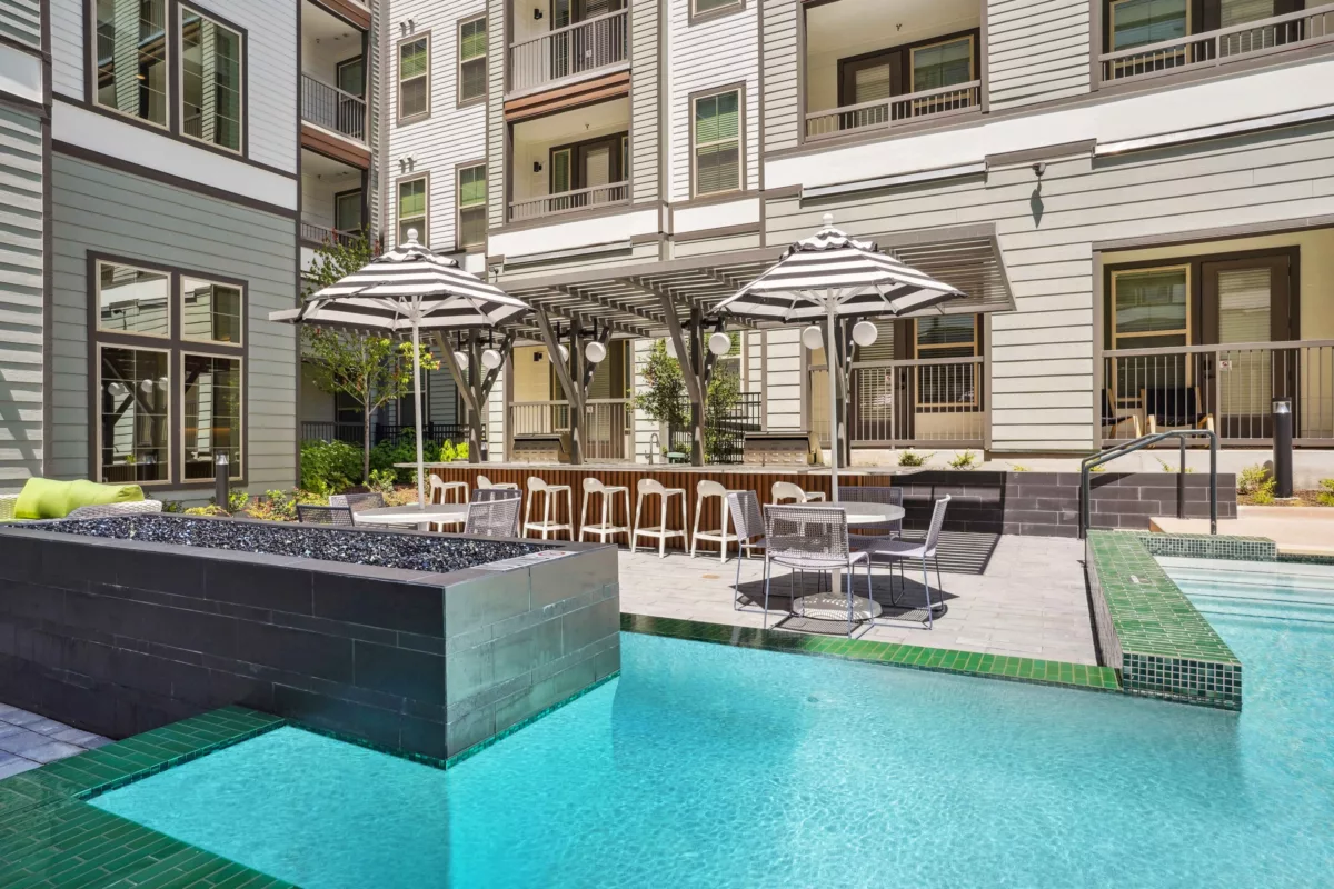 Outdoor pool area with bar, seating, and fire feature. Building facade in background.