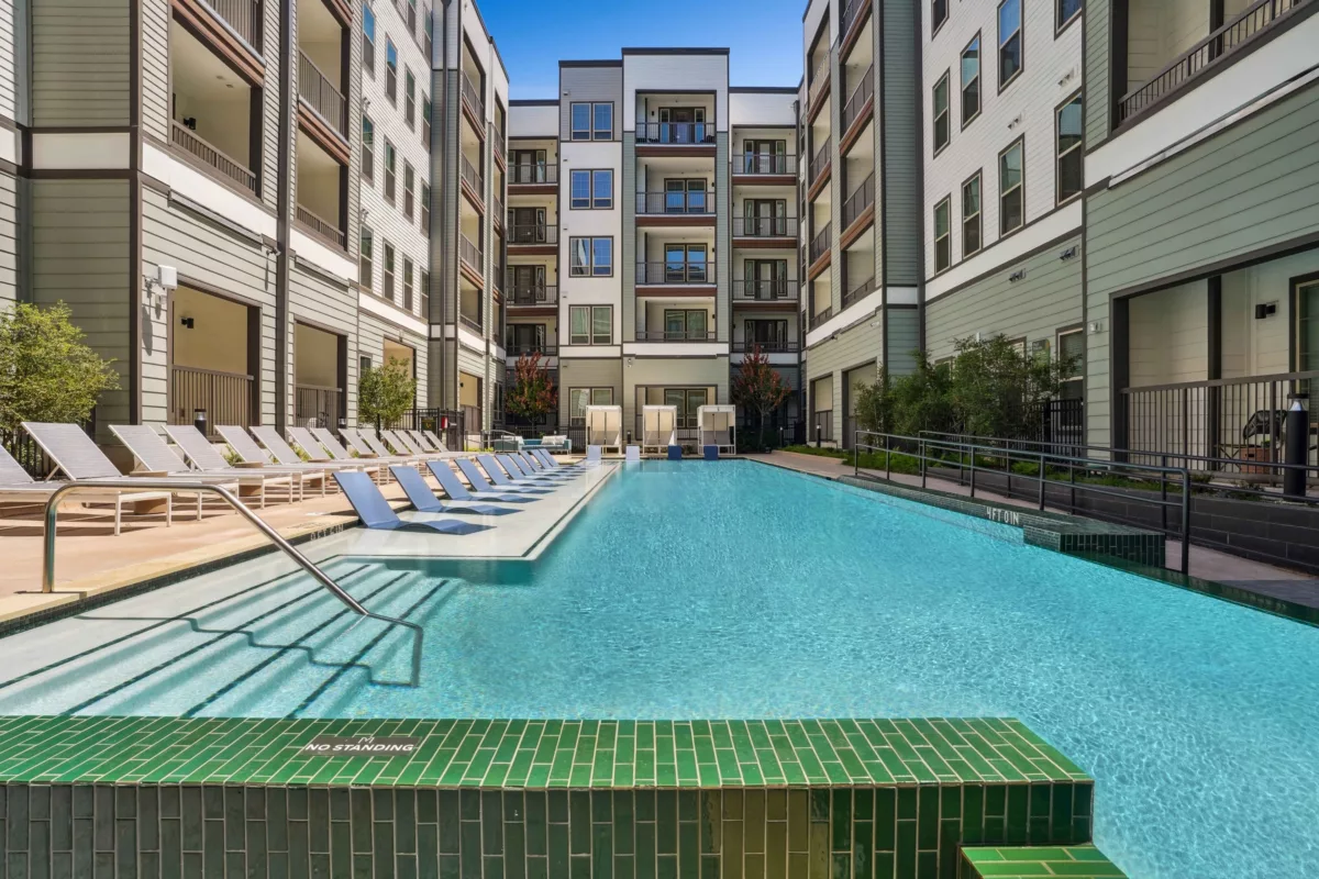 Resort-style pool with lounge chairs, surrounded by multi-story buildings with balconies.
