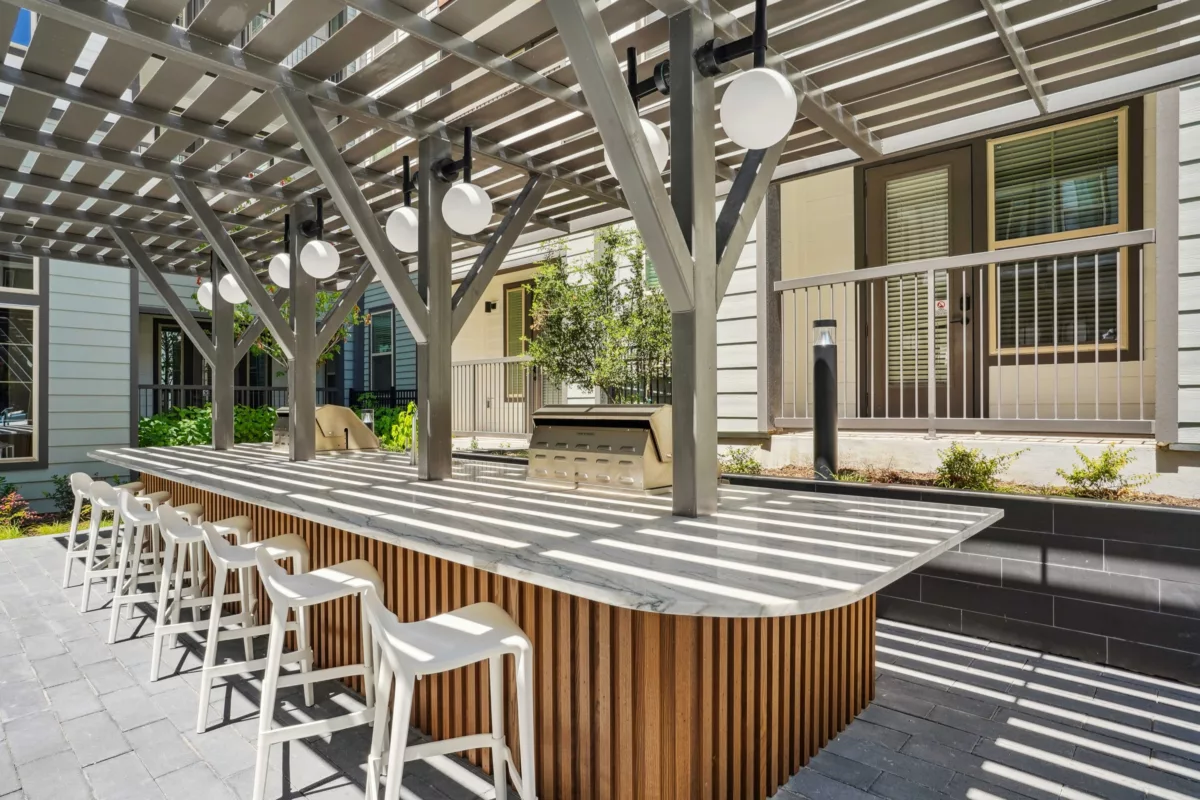 Outdoor grilling area with marble countertop, wood base, stools, and overhead pergola.