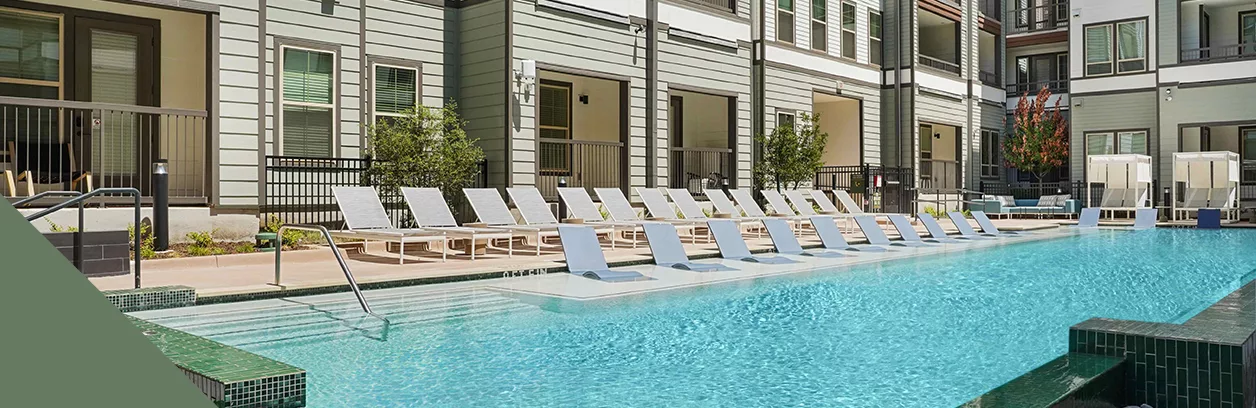 A pool with lounge chairs in the water and on the pool deck in the courtyard of an apartment building.