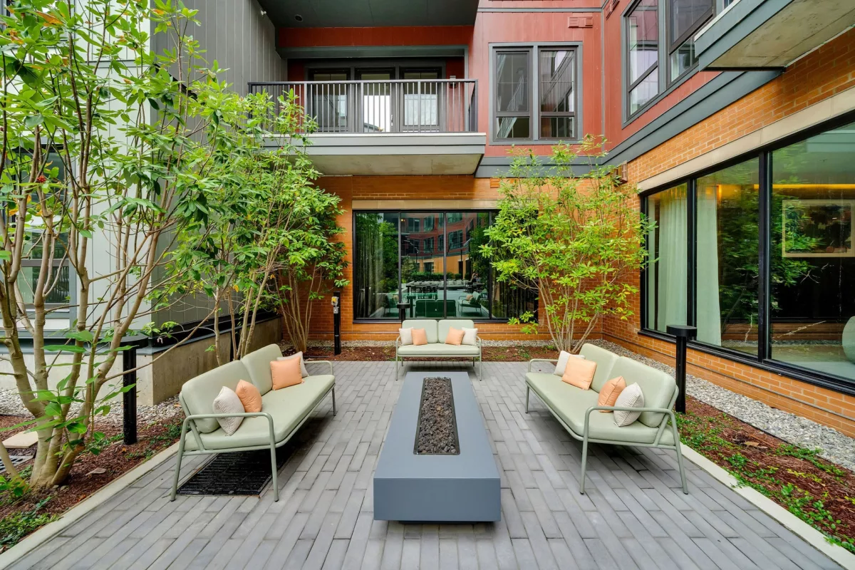 Outdoor courtyard with benches, throw pillows, fire pit, and landscaping. Brick and metal building.