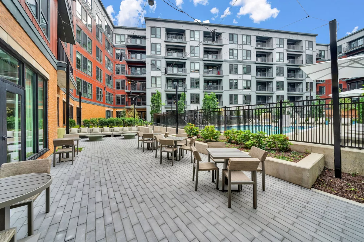Outdoor patio with tables, seating, and pool view between buildings.