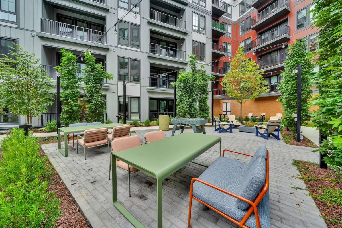 Outdoor courtyard with tables, chairs, foosball, and string lights between apartment buildings.