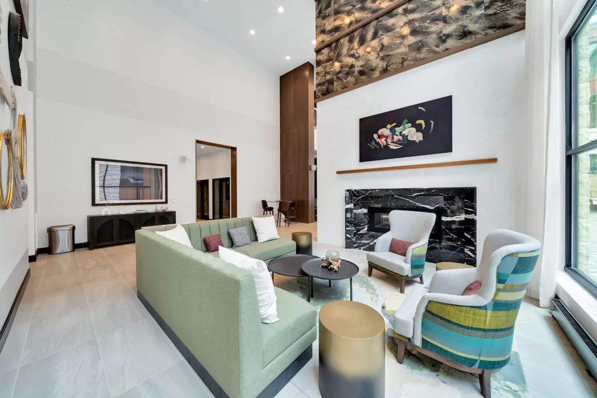 Lounge with green sofa, chairs, fireplace, and artwork in a high-ceilinged room.
