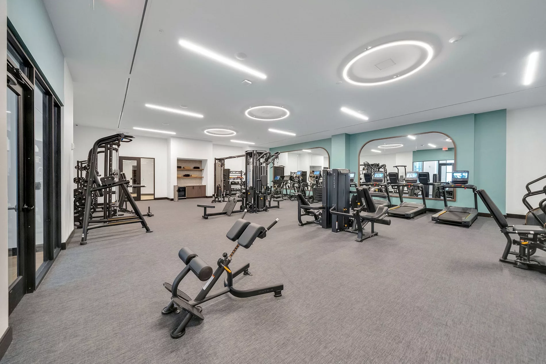 Fitness center with treadmills, weight machines, and mirrored wall. Gray carpet flooring.