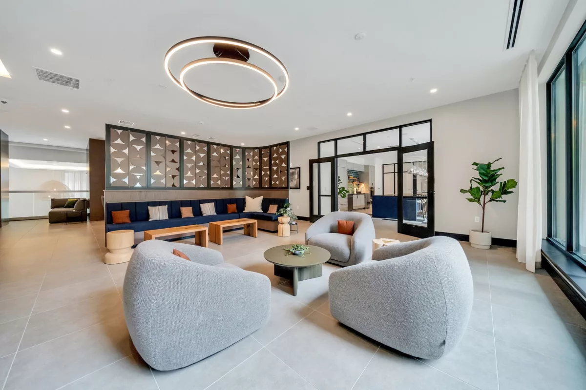 Modern lounge with gray chairs, blue sofa, and decorative screen. Large windows provide natural light.