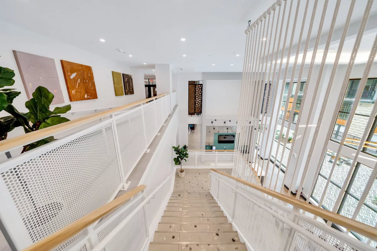 View down open staircase with white railings, light wood handrails, and art on the wall.