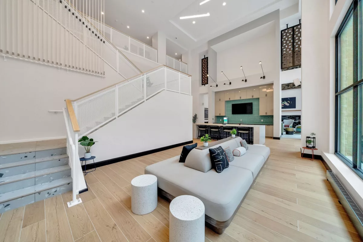 Modern lounge with a large sofa, kitchen, and staircase. Bright, open space.