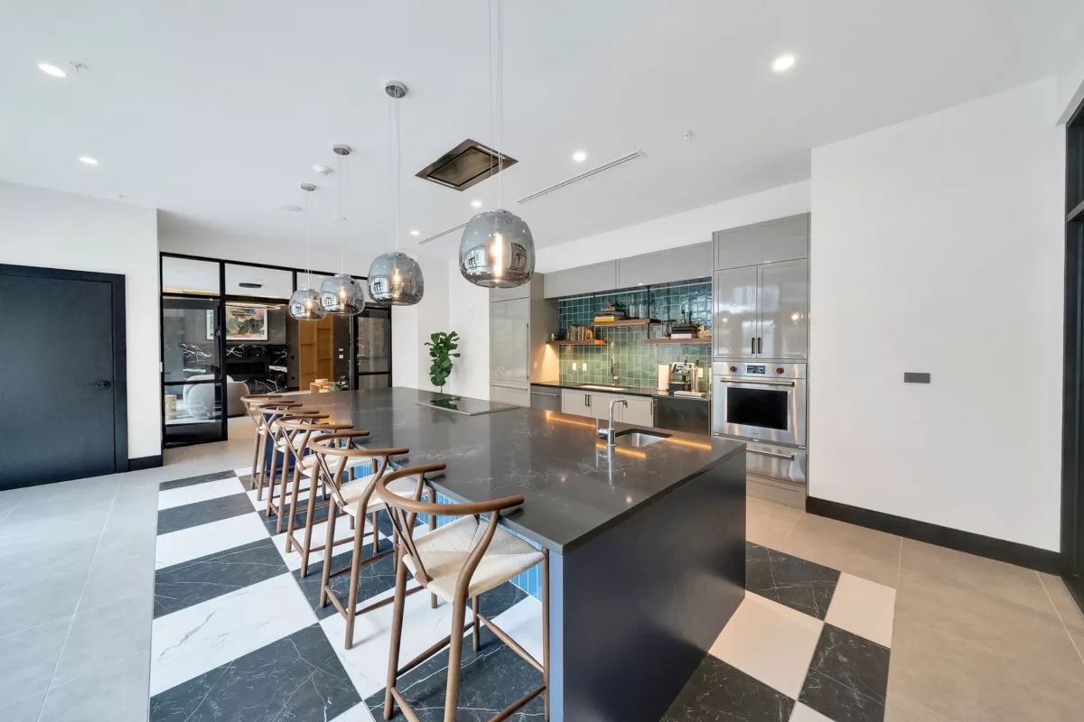 Modern kitchen with gray cabinets, island with seating, and black and white checkered floor.