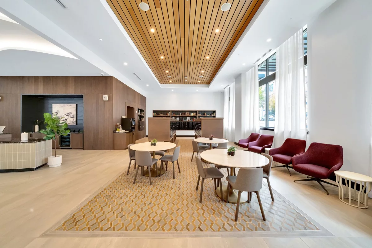 Lounge area with tables, chairs, wood ceiling, and large windows with sheer white curtains.