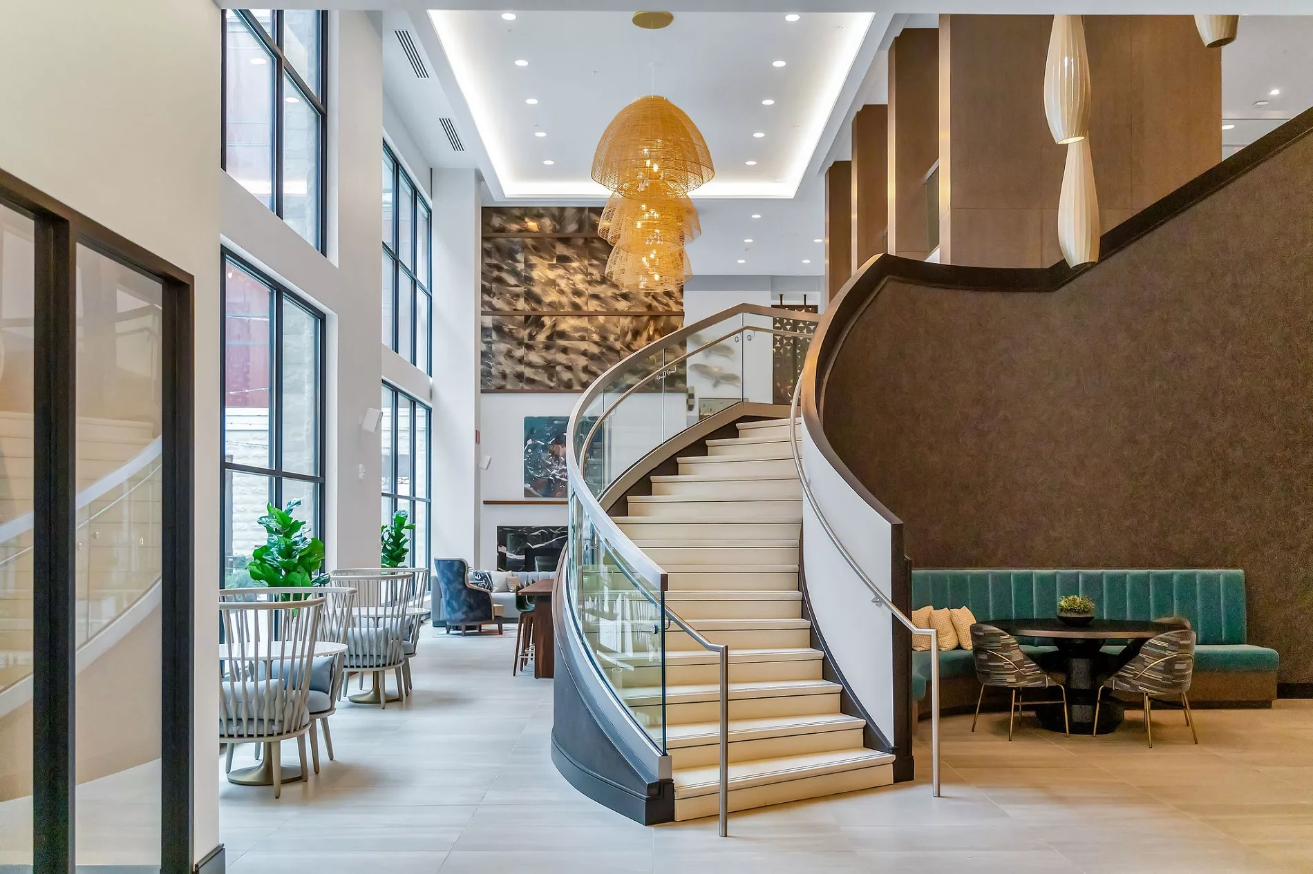 Grand lobby with curved staircase, seating areas, and modern chandelier.