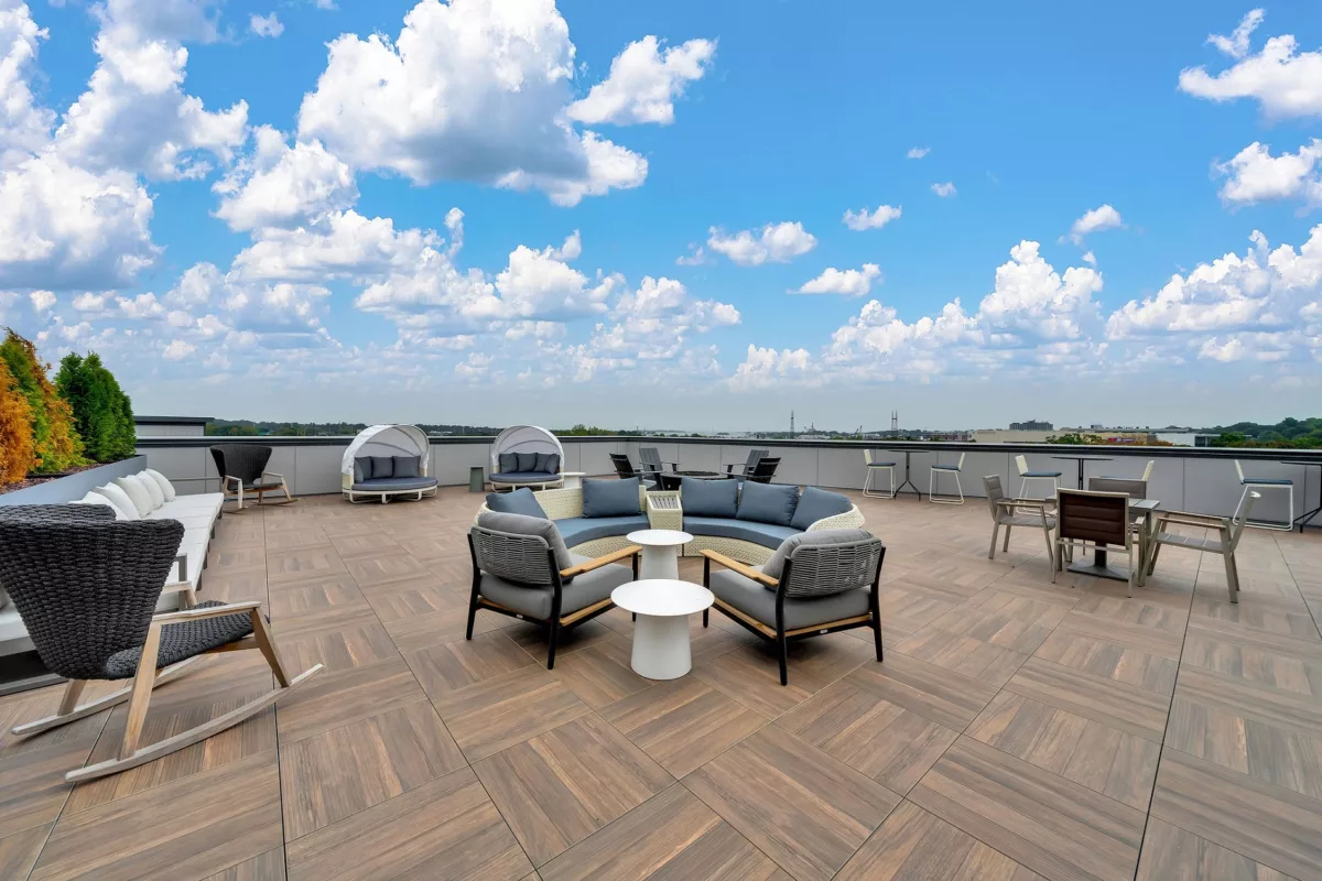 Rooftop lounge with seating, tables, and city views under a blue sky.