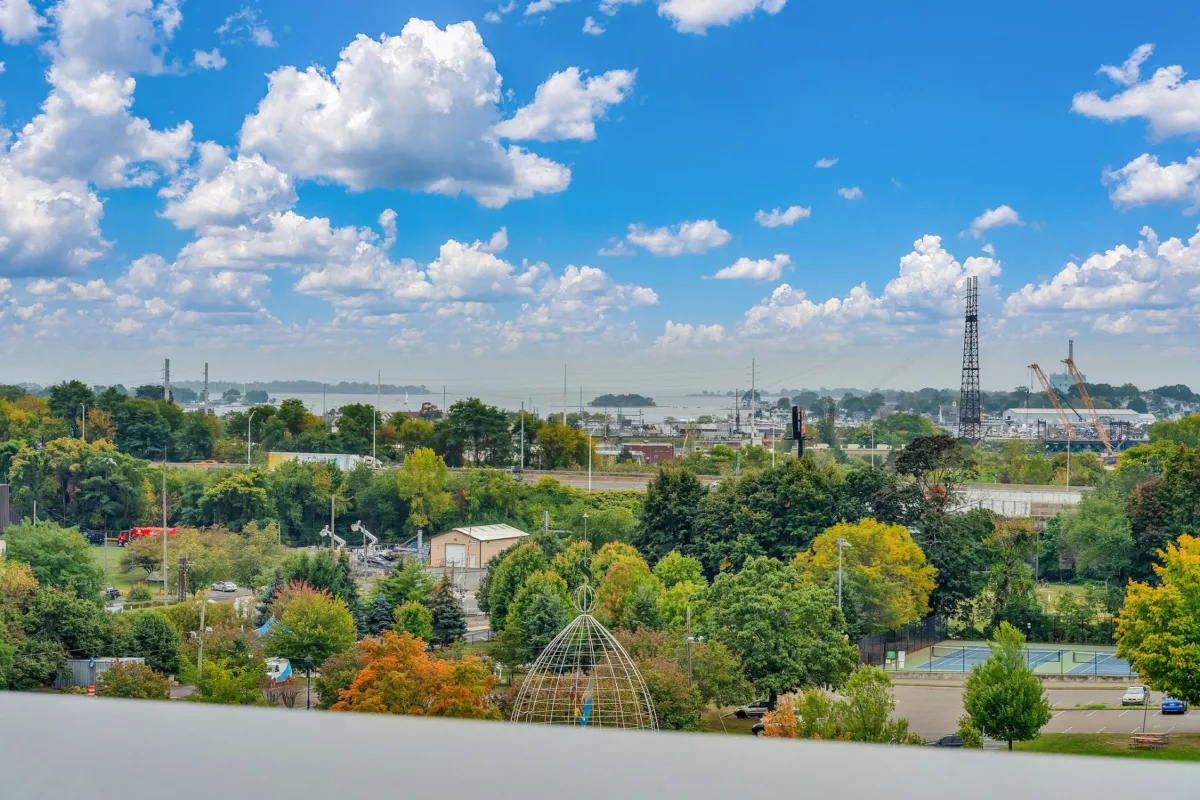 View of city skyline, water, and trees under a blue, cloudy sky from a high vantage point.