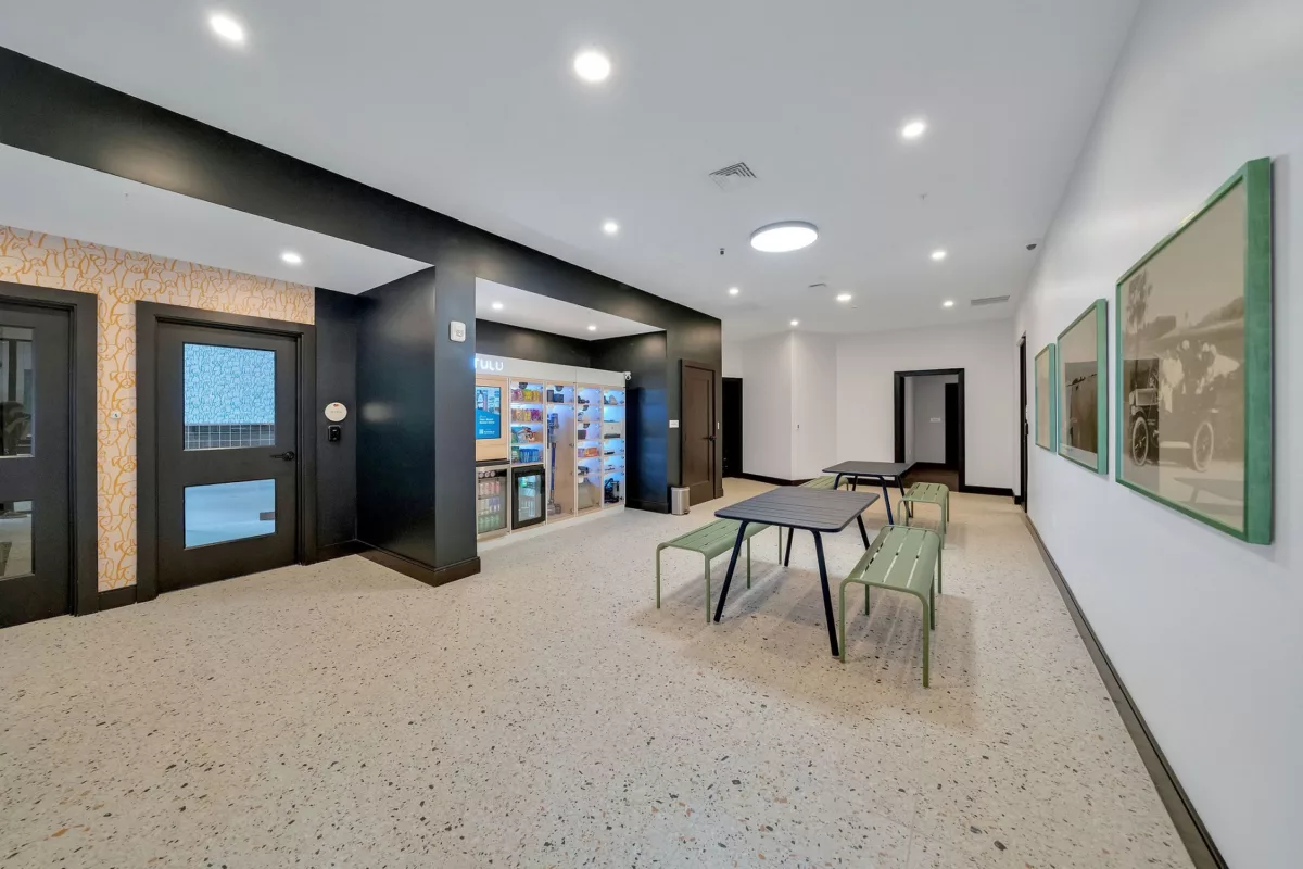 Lounge area with vending machine, tables, benches, and framed artwork on a white wall.