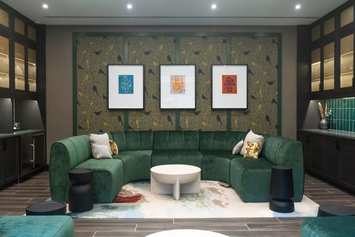 Lounge area with green velvet sectional, art, and dark cabinetry.