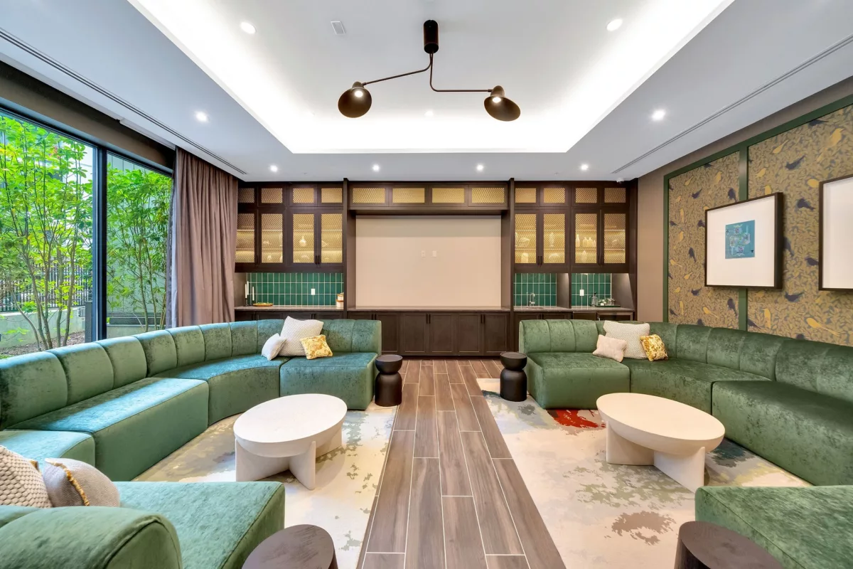Lounge area with green sofas, wood floors, and kitchenette. Large window with outdoor view.