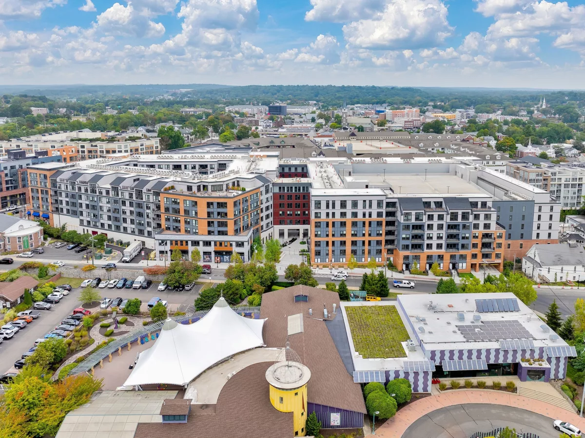Aerial view of multi-story buildings, parking, and surrounding cityscape under a partly cloudy sky.