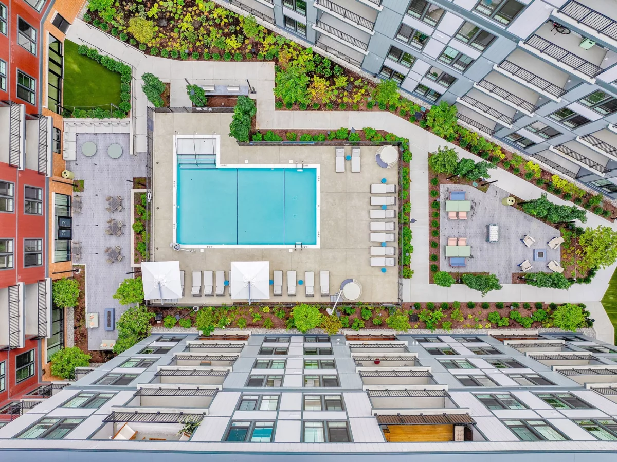 Aerial view of pool, lounge chairs, and patio areas between apartment buildings.